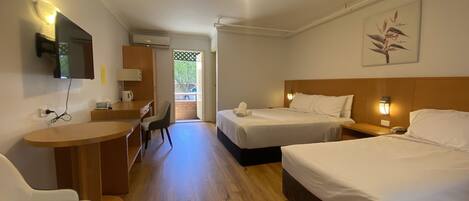 Habitación de hotel con dos camas, un escritorio, una silla, un televisor montado en la pared y una puerta que da a un espacio exterior.