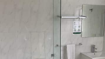 A modern bathroom with a glass-enclosed shower, a freestanding bathtub, a white vanity with a mirror, and a towel rack.
