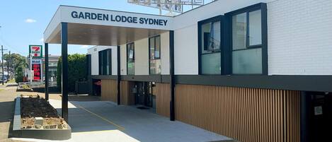 A modern building with a sign reading "Garden Lodge Sydney" and a 7-Eleven convenience store nearby.