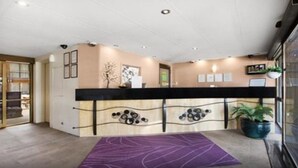 Zona de recepción con mostrador, una alfombra morada y una planta en maceta.