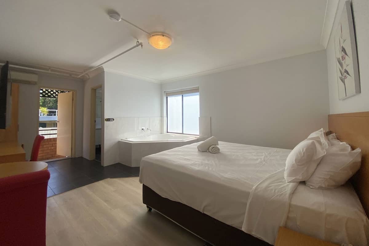 A hotel room with a bed, a window, a bathroom, and a door leading to a balcony.