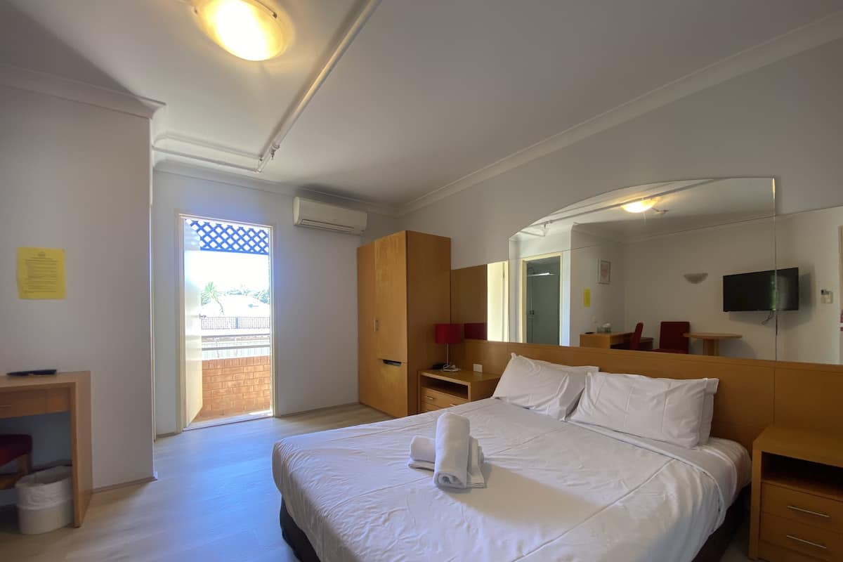 A hotel room with a large bed, a wooden wardrobe, a desk with a chair, a television, and a mirror.