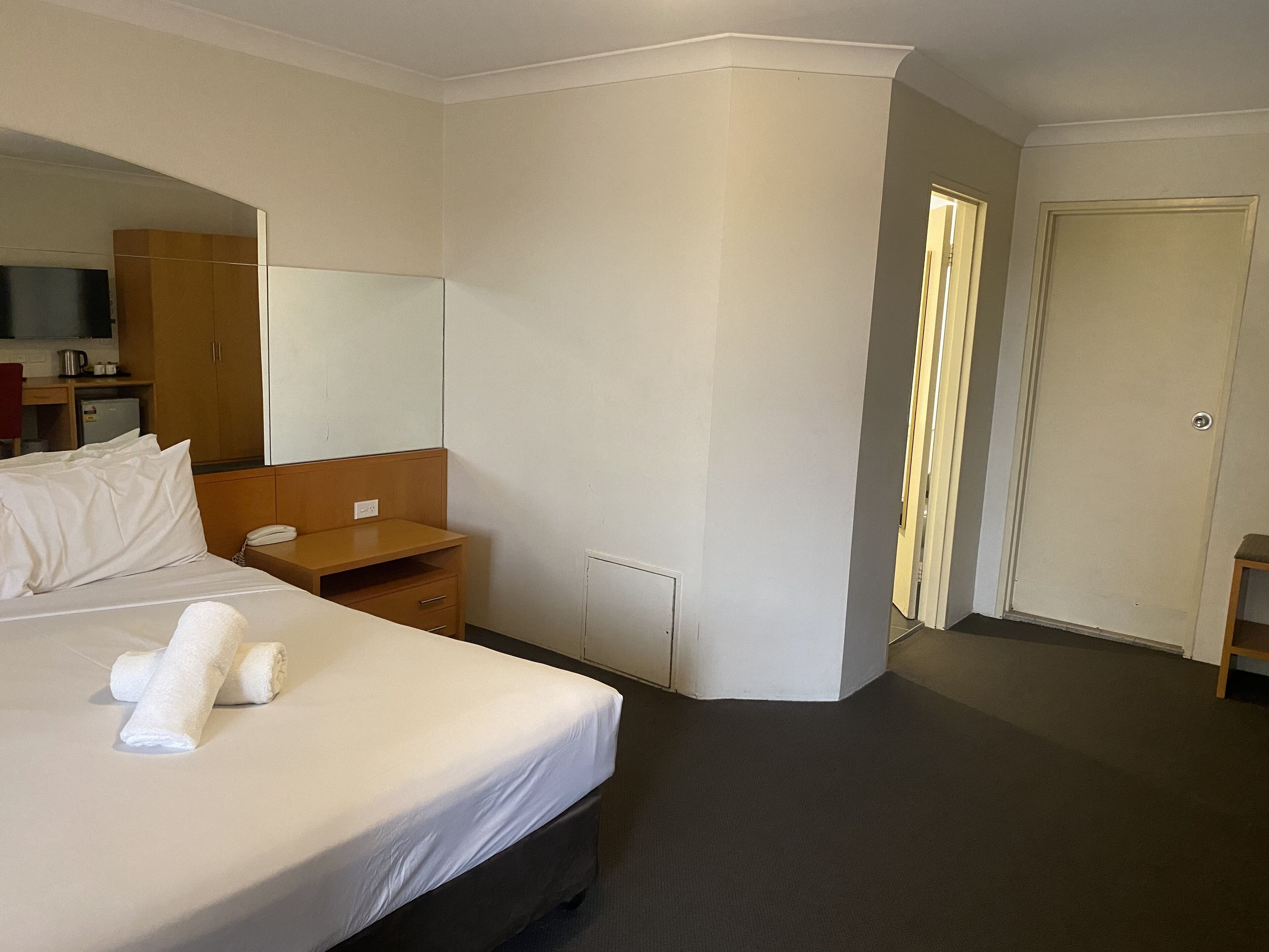 Habitació d'hotel amb llit, taulella de nit, mirall, armari, escriptori amb cadira i una porta.
