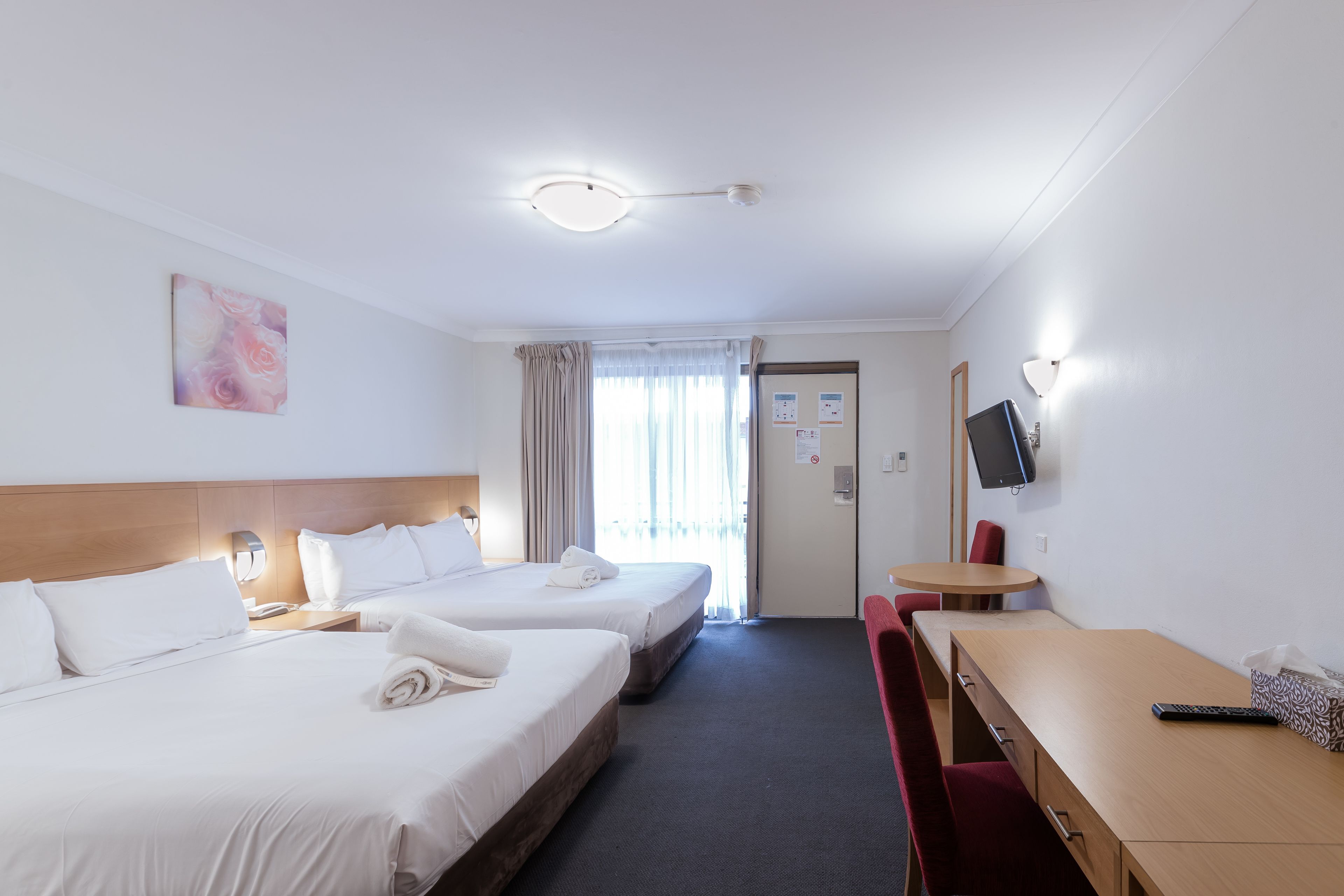 A hotel room with two beds, a desk, a chair, a TV, and a window with curtains.
