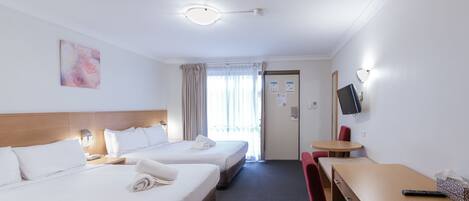 A hotel room with two beds, a desk, a chair, a TV, and a window with curtains.
