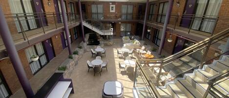 A spacious indoor atrium with multiple levels, featuring a central staircase, seating areas, and a glass ceiling.