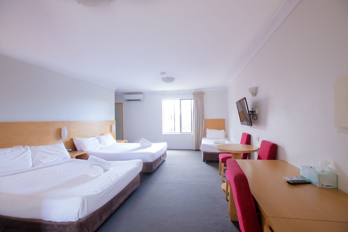 A hotel room with two beds, a small table, a chair, and a window.