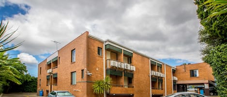 A multi-story brick building with a parking lot, two cars parked, and a small palm tree.