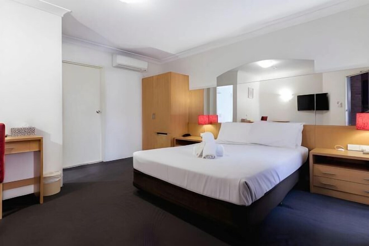 A hotel room with a bed, bedside tables, a desk, a mirror, and a television.