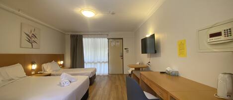 Habitación de hotel con dos camas, un escritorio, una silla, un televisor y una cafetera.