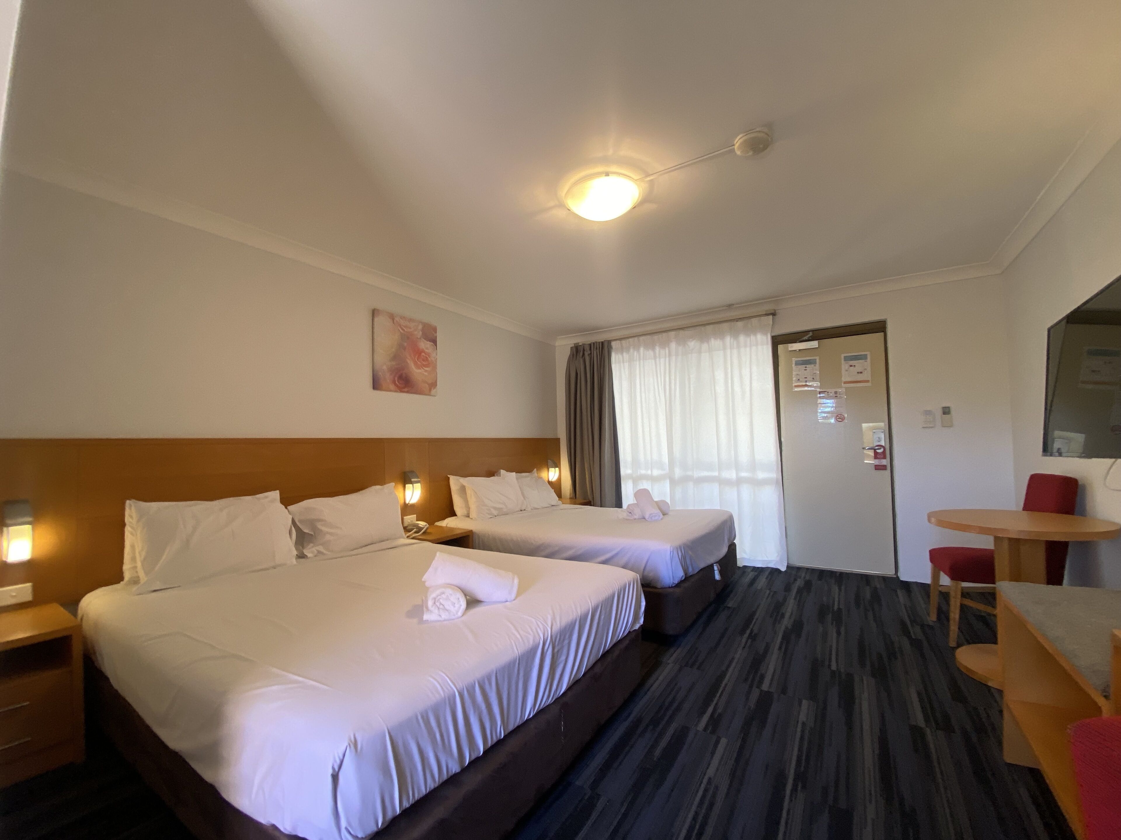 A hotel room with two beds, a desk, a chair, and a small table.