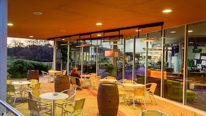 An outdoor seating area with tables and chairs, large wooden barrels, and glass walls offering views of the interior.