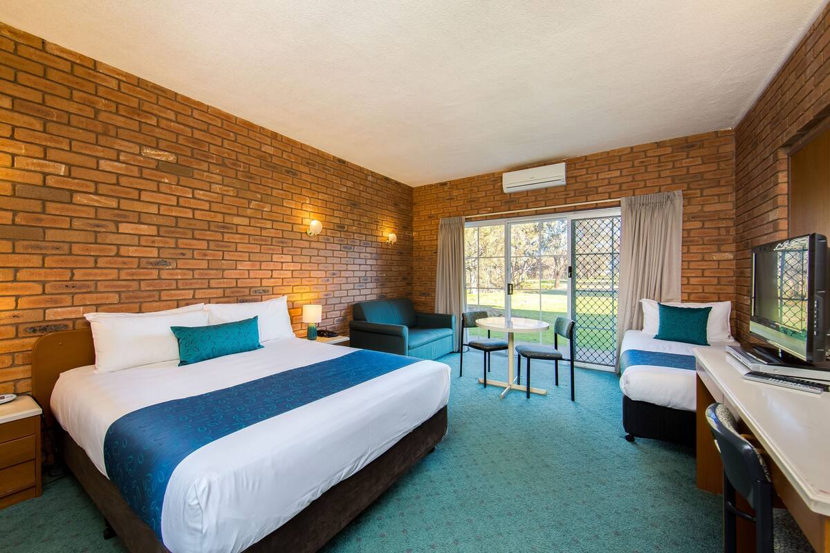 A hotel room with a brick wall, a large bed, a desk with a computer, a TV, and a small table with chairs.