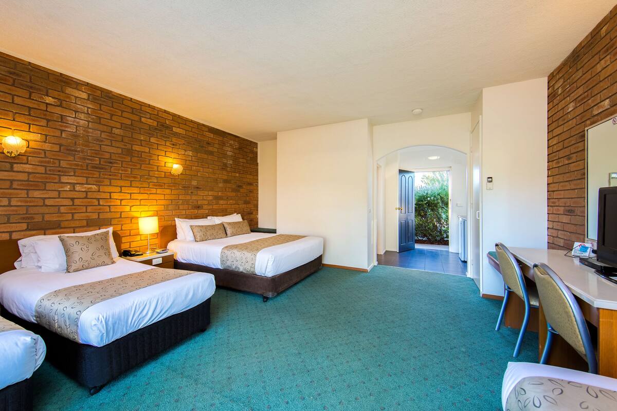 A hotel room with two beds, a desk, and a TV.