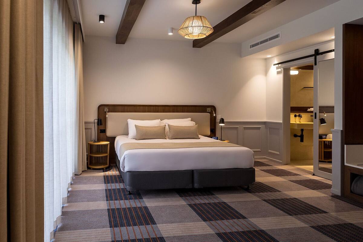 A modern hotel room with a large bed, a bedside table, a lamp, and a view of the bathroom.