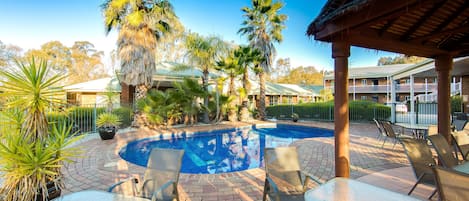 A pool area with lounge chairs and a covered seating area.