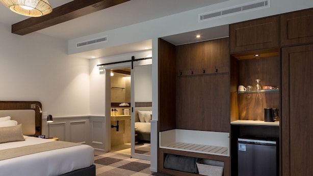 A hotel room with a bed, a small kitchenette, a walk-in closet, and a bathroom with a shower and toilet.