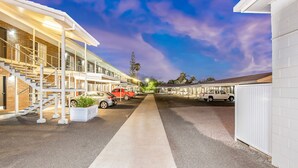 A row of motel-style buildings with a central walkway, outdoor parking, and a clear sky. - Takalvan Motel (Bundaberg West)