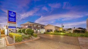 A well-lit motel with a large signboard, a paved driveway, and neatly trimmed hedges. - Takalvan Motel (Bundaberg West)