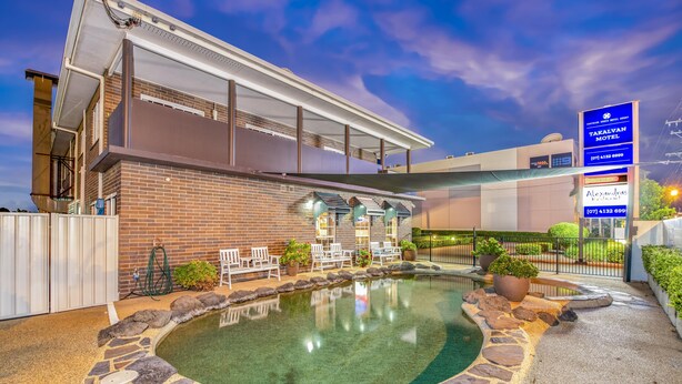 A modern building with a pool area, outdoor seating, and a sign for Takalvan Motel. - Takalvan Motel (Bundaberg West)