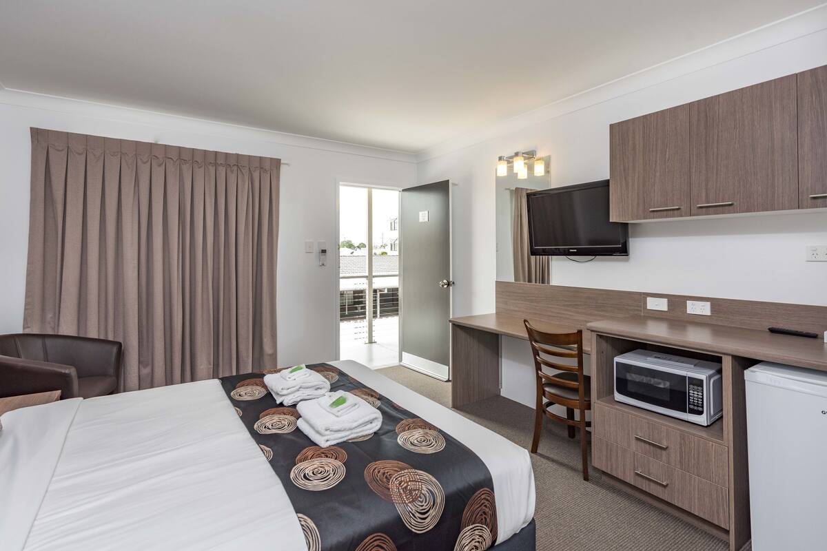 Habitación de hotel con cama, escritorio, microondas, televisión y puerta corrediza a un balcón.