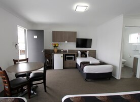 Una habitación compacta con mesa, sillas, cama, kitchenette pequeña y televisor.