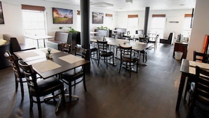 A spacious dining area with multiple tables and chairs, large windows with blinds, and a mix of seating options including booths and individual tables. - Takalvan Motel (Bundaberg West)