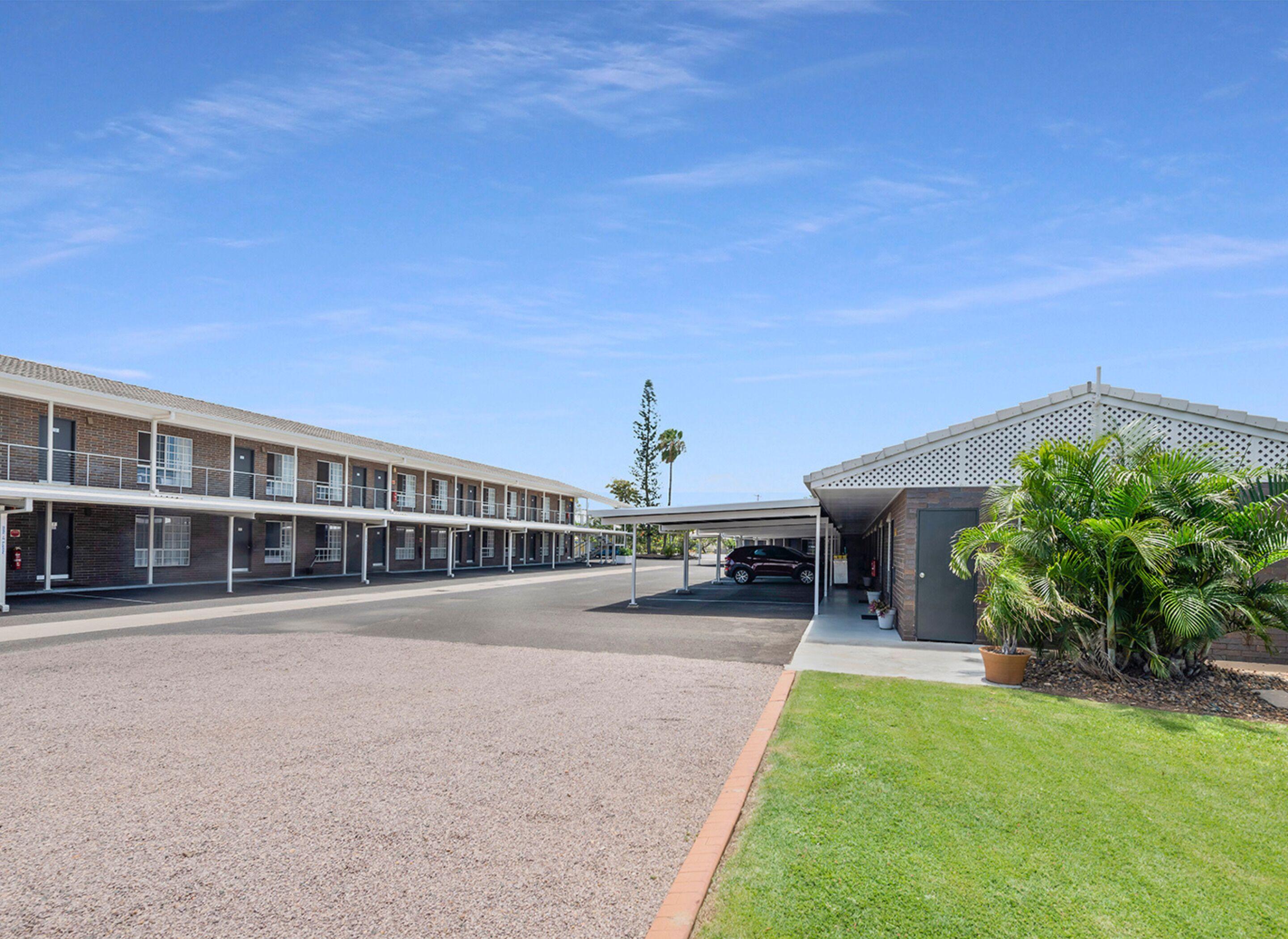 A motel with a covered parking area and a small garden with palm trees.