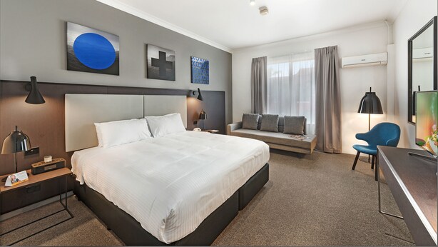 Ein modernes Hotelzimmer mit einem großen Bett, einem Schreibtisch, einem Sessel und einer Couch.