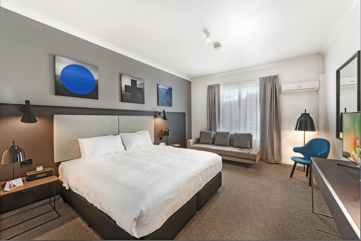 Une chambre d’hôtel moderne équipée d’un grand lit, d’un bureau, d’une chaise et d’un canapé.