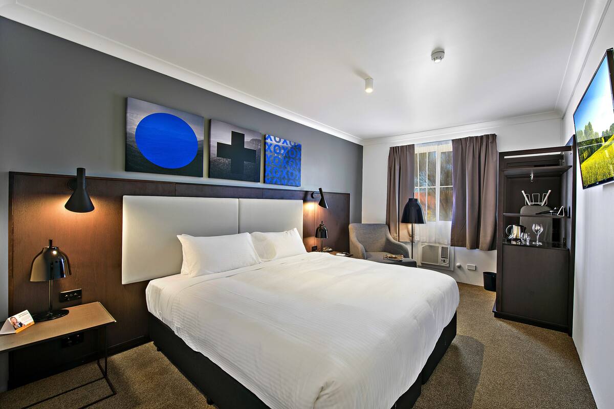 Une chambre d’hôtel avec un grand lit, un bureau, une chaise, une armoire et des œuvres d’art accrochées au mur.