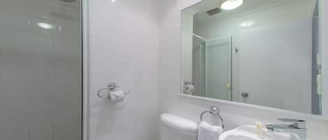 Un baño moderno con ducha de vidrio, inodoro blanco y lavamanos con espejo.