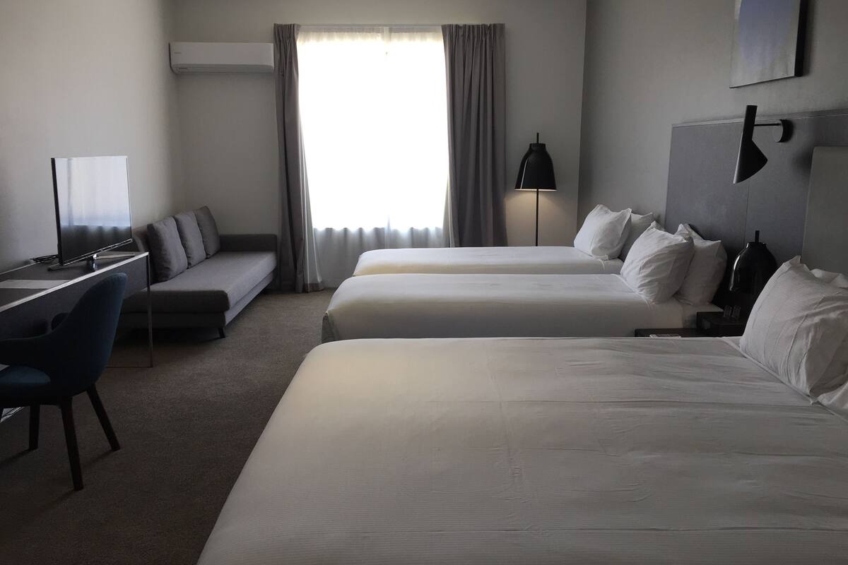 Une chambre d’hôtel avec deux lits, un bureau, une chaise, une lampe et une fenêtre avec des rideaux.