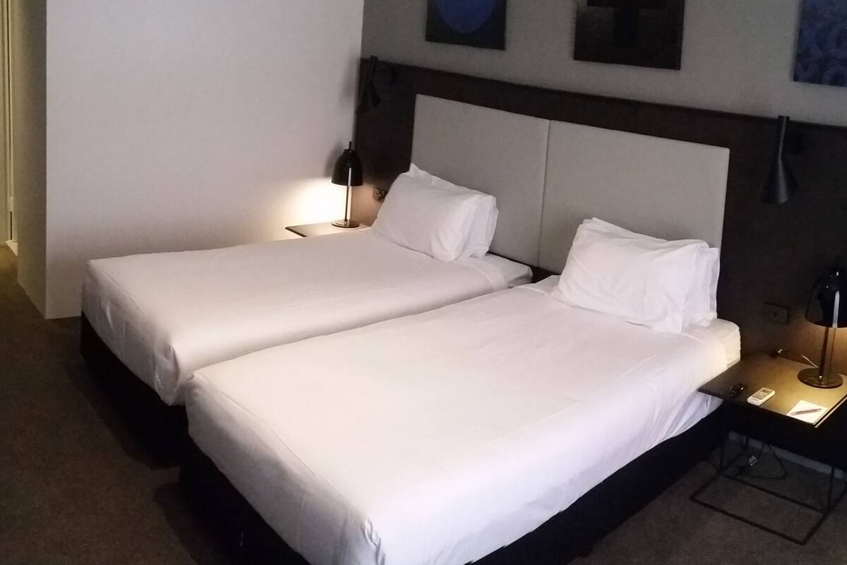 Une chambre d’hôtel avec deux lits simples, un bureau avec une lampe, une chaise et une armoire.