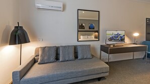 Ein modernes Zimmer mit grauem Sofa, Schreibtisch mit Computer und Lampe, Spiegel und Klimaanlage.