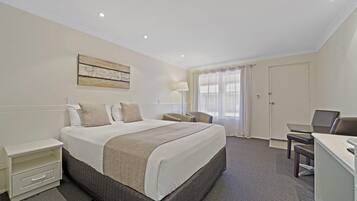 A hotel room with a large bed, a desk, a chair, a nightstand, and a lamp.