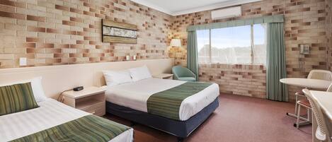 Habitación de hotel con dos camas, un escritorio, una silla, una ventana con cortinas y una pared de ladrillo.