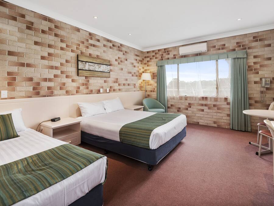 Habitación de hotel con dos camas, un escritorio, una silla, una ventana con cortinas y una pared de ladrillo.