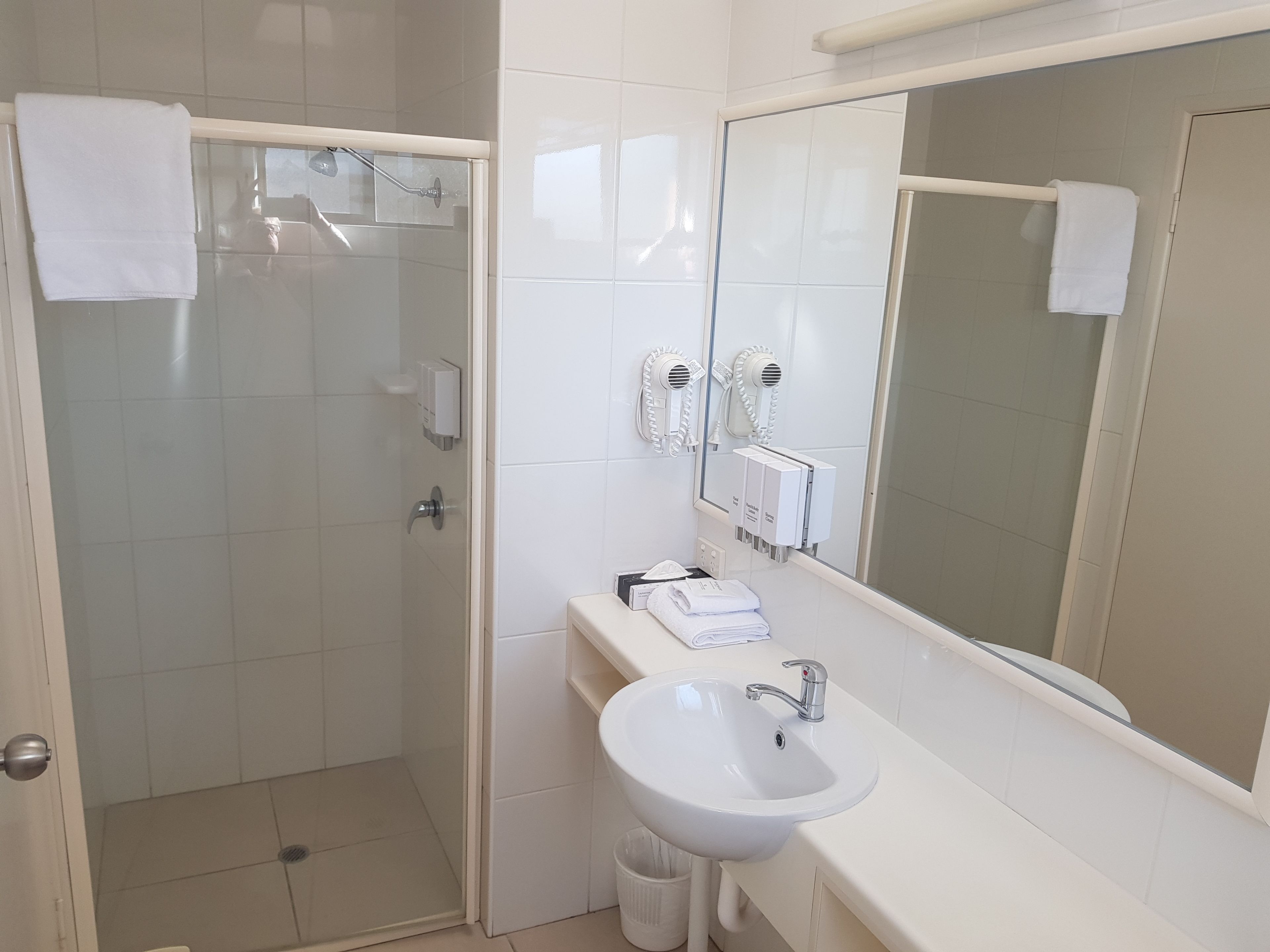 A bathroom with a glass-enclosed shower, a white sink, and a large mirror.