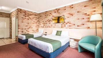 Une chambre d’hôtel avec deux lits, un mur décoré d’un motif en briques, un tableau, une lampe et un fauteuil de couleur turquoise.