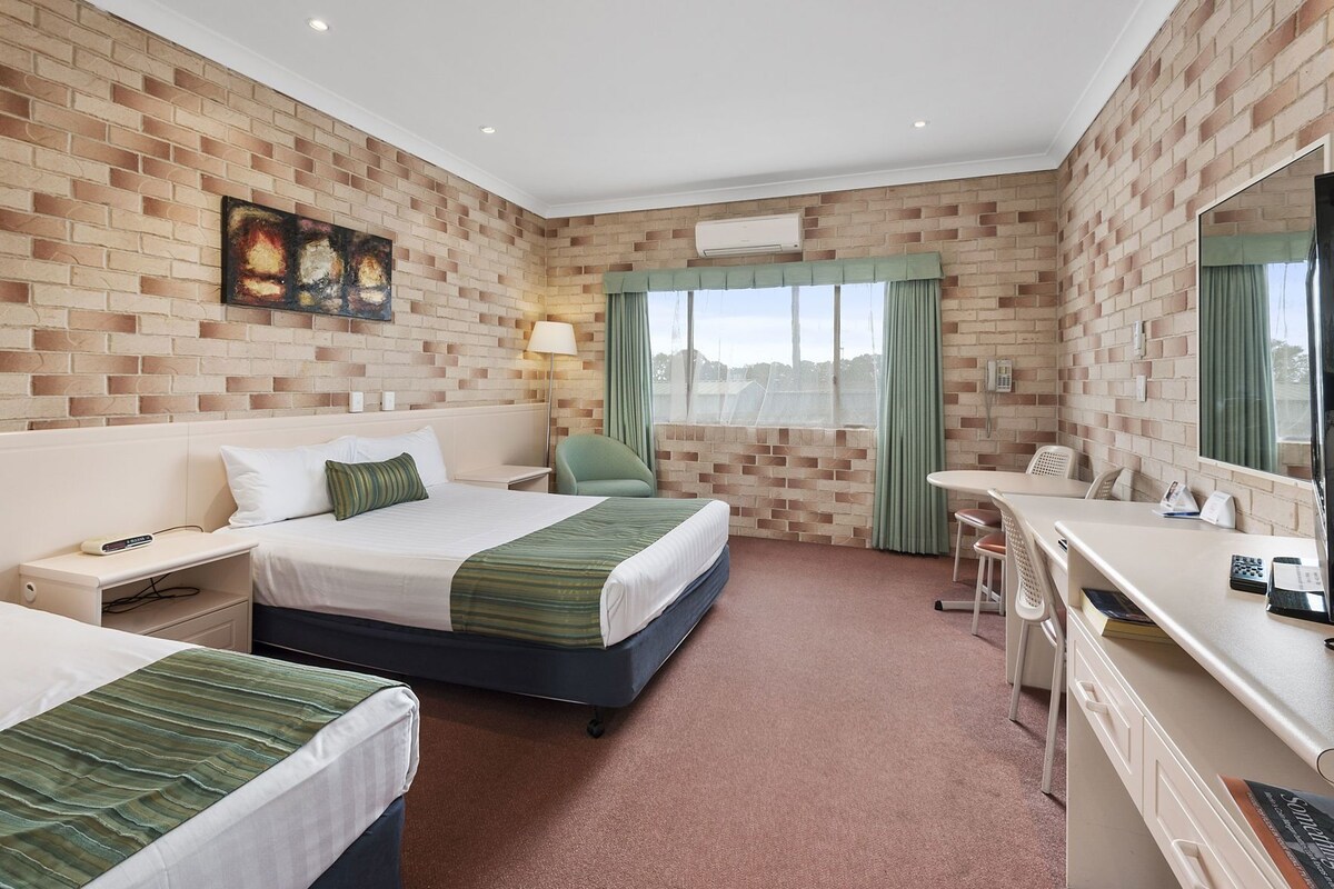 A hotel room with two beds, a desk, a chair, and a large window with curtains.