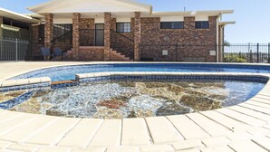 Una piscina con borde de losa de piedra, una casa de ladrillo con techo blanco y una valla de metal negro.