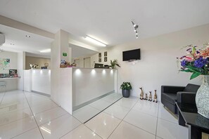 A clean, modern reception area with a reception desk, a flat-screen TV, and a seating area with a sofa and a table. - Comfort Inn Glenfield (Kearneys Spring)