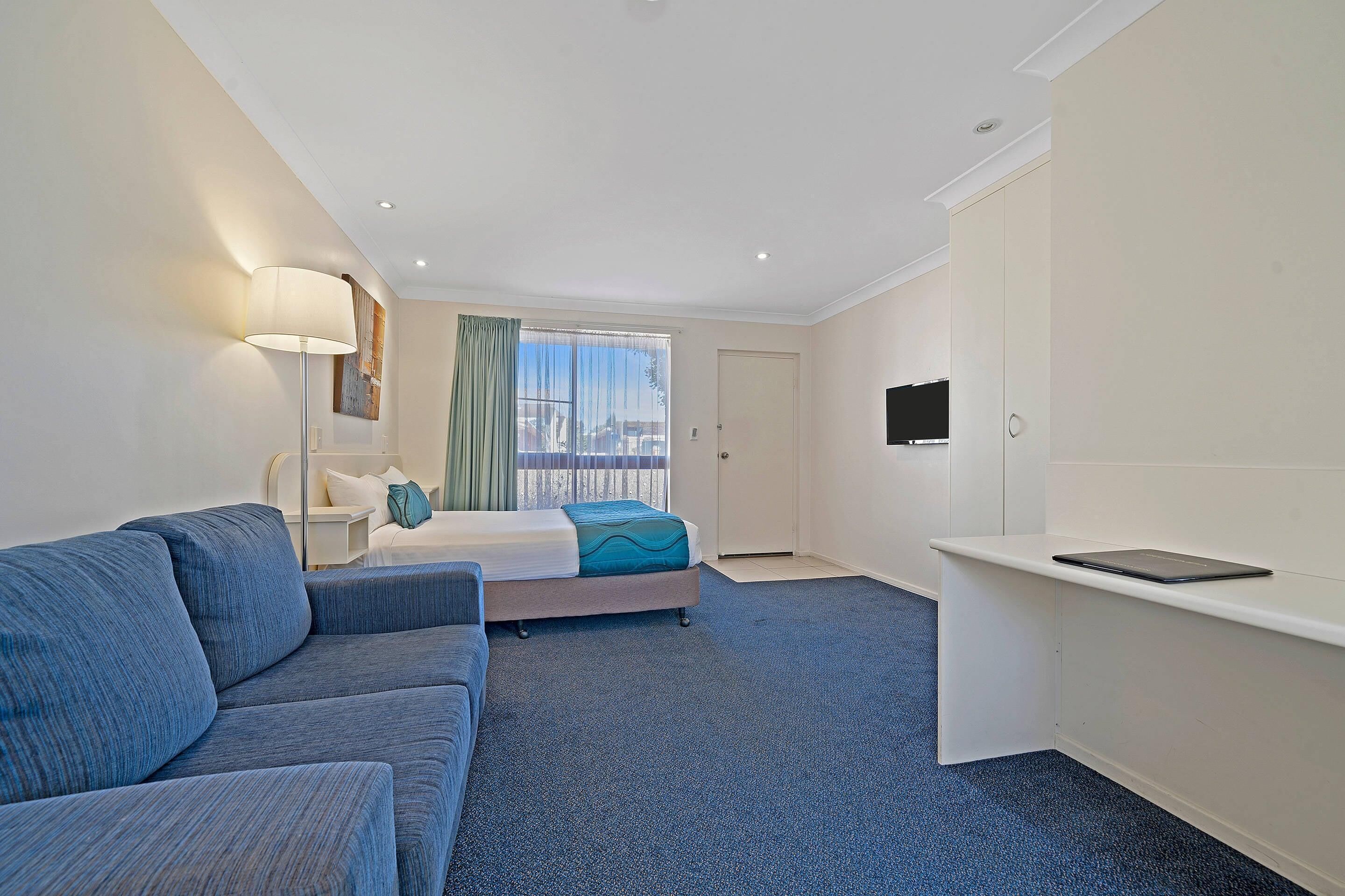 Une chambre d’hôtel avec un lit, un canapé, un bureau, une télévision et une fenêtre avec des rideaux.