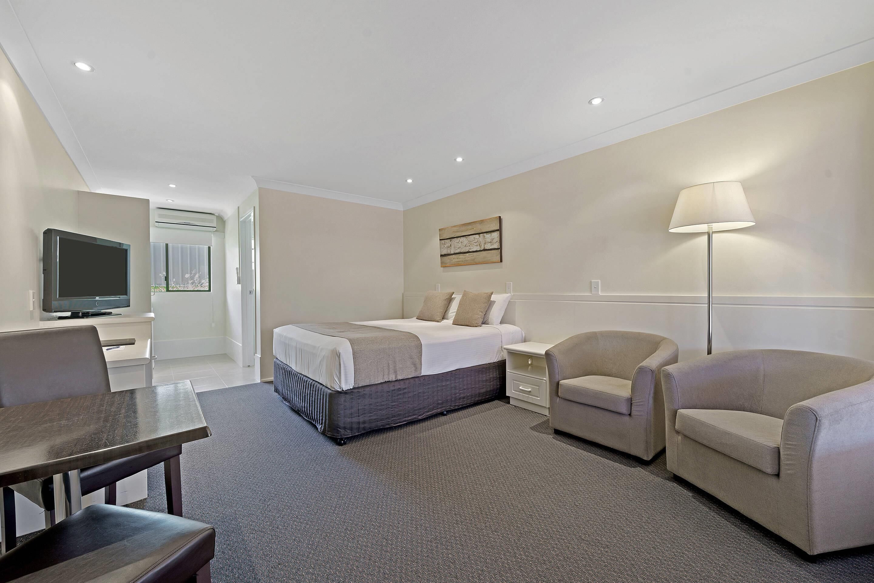 A hotel room with a bed, a desk, a chair, a sofa, and a TV.