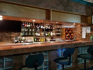 A bar area with a wooden counter, shelves of liquor bottles, glasses, and a wine rack. There are three bar stools and a TV mounted on the wall. - Comfort Inn Glenfield (Kearneys Spring)