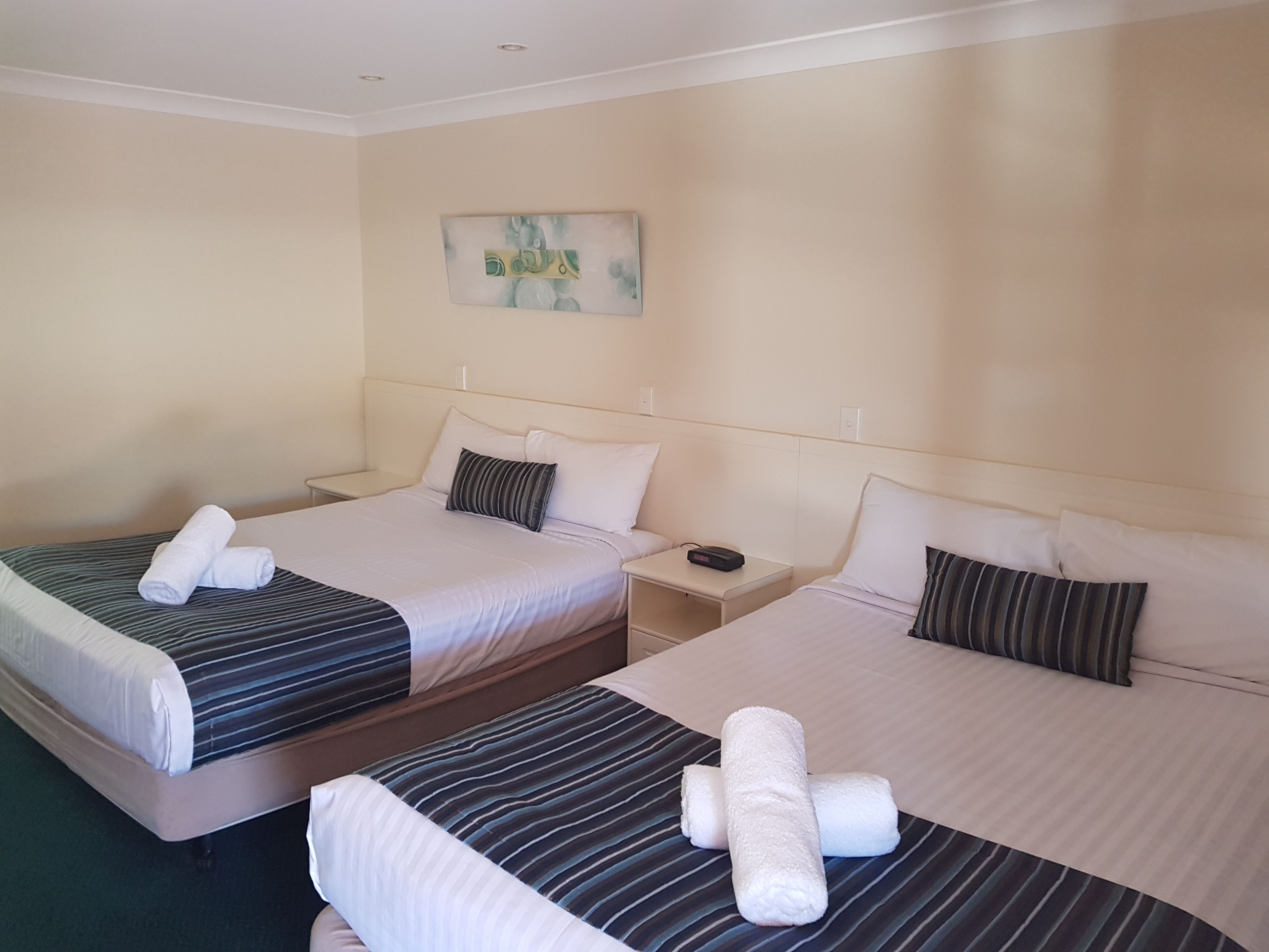 A hotel room with two beds, each with striped bedding and rolled towels. There is a nightstand between the beds, and a painting on the wall.