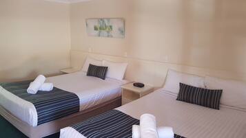 A hotel room with two beds, each with striped bedding and rolled towels. There is a nightstand between the beds, and a painting on the wall.