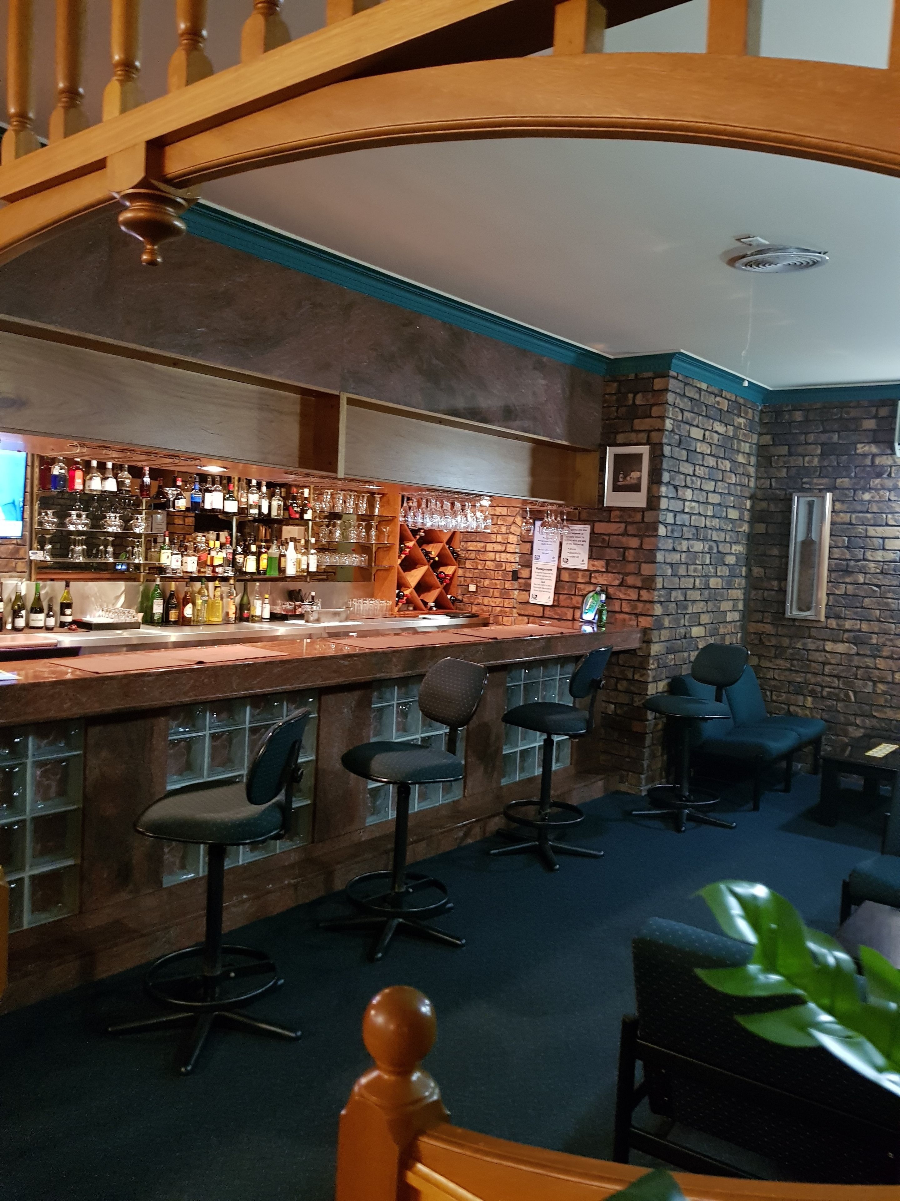 A bar area with a wooden bar counter, multiple stools, and a brick wall.