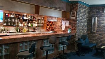 A bar area with a wooden bar counter, multiple stools, and a brick wall.